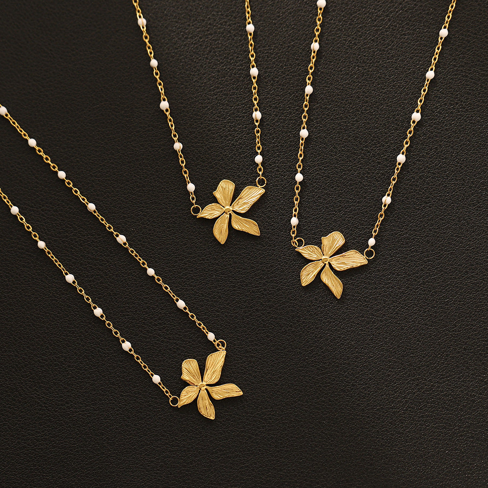 three gold plated floral necklaces with white bead accents on a black background