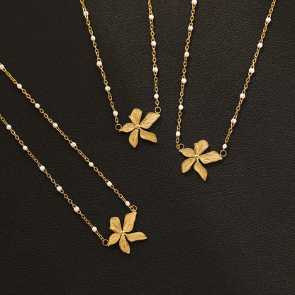 three gold plated floral necklaces with white bead accents on a black background