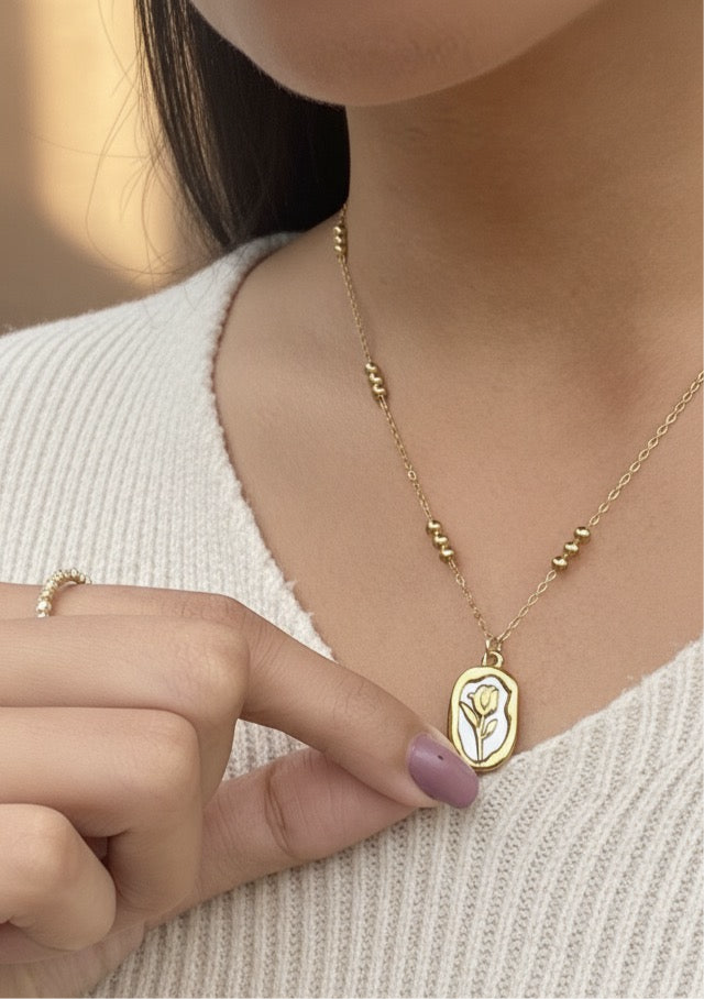 Lilyah Jewelry Necklace. Rose or Tulip 
Gold necklace with a pendant worn by a person, with a blurred background. 