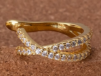 An 18k gold plated and zircon studded ear cuff, non piercing earing. Adorned with clear round-cut zircons, displayed on a textured brown surface.