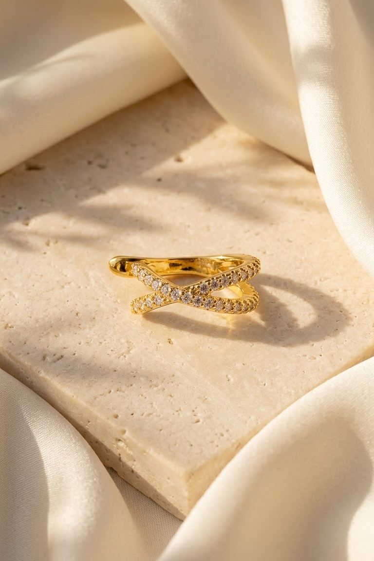 Lilyah Jewelry's 18k gold plated ear cuff with pavé-set clear zircons, styled on a textured beige stone slab surrounded by draped cream-colored fabric under warm sunlight.