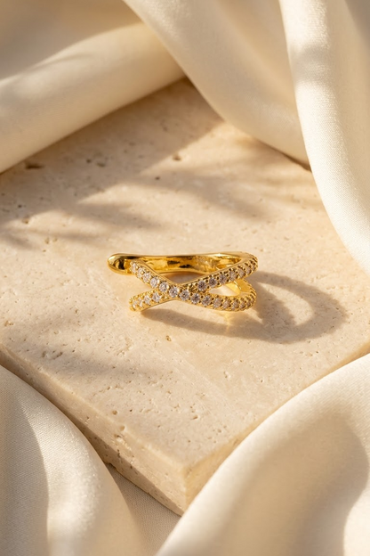 Lilyah Jewelry's 18k gold plated ear cuff with pavé-set clear zircons, styled on a textured beige stone slab surrounded by draped cream-colored fabric under warm sunlight.
