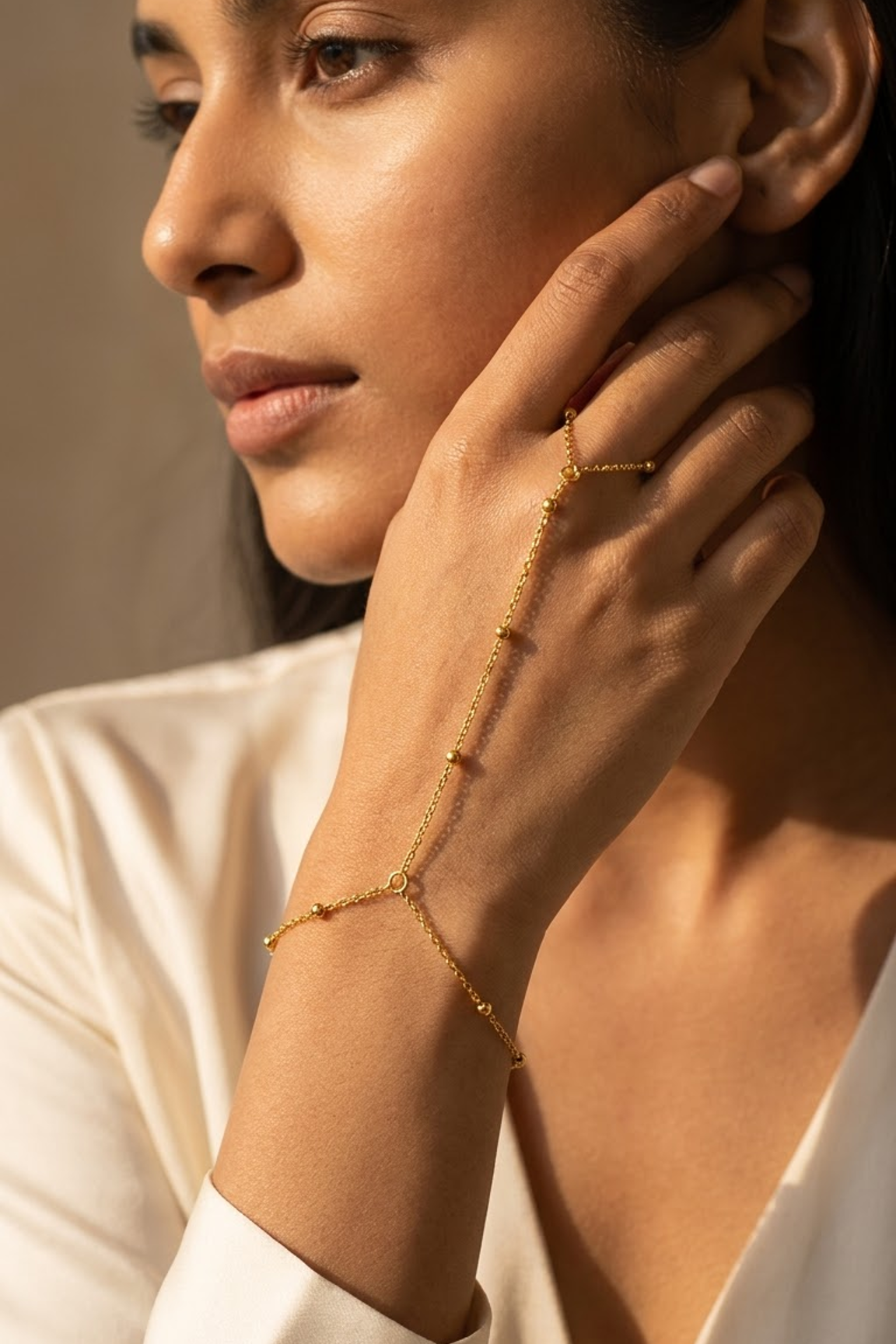 A close-up lifestyle shot of a woman wearing Lilyah Jewelry's delicate gold plated bracelet and matching delicate gold chain wrist bracelet, styled with a white satin blouse.