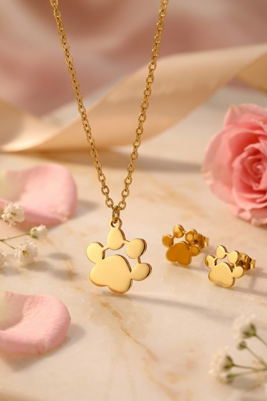 Lilyah Jewelry's Gold plated paw print necklace and matching stud earrings displayed on a marble surface with pink rose petals and small white flowers.