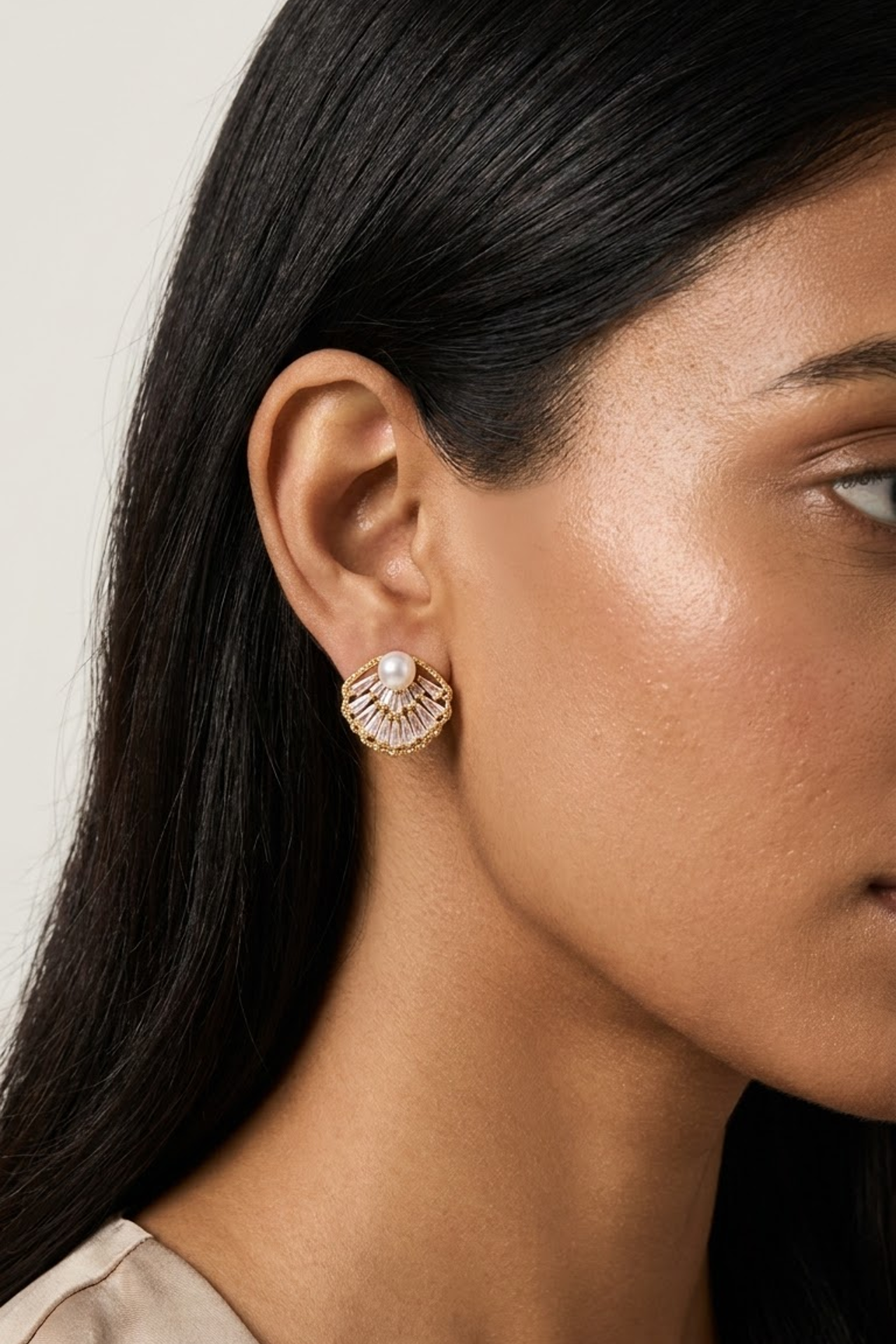 A close-up side profile of a woman wearing an 18k gold plated shell-shaped stud earring with a central white pearl from Lilyah Jewelry, set against a neutral light gray background.