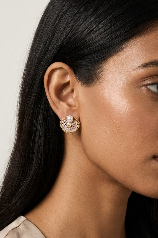 A close-up side profile of a woman wearing an 18k gold plated shell-shaped stud earring with a central white pearl from Lilyah Jewelry, set against a neutral light gray background.