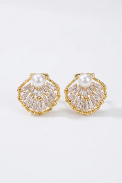 A pair of 18k gold-toned shell-shaped earrings with a white pearl at the center and clear baguette crystals radiating from the edges, shown on a clean white background.