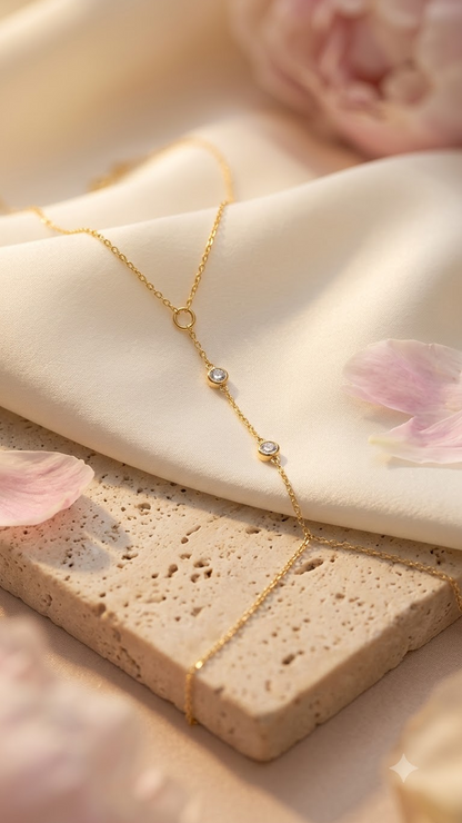 Lilyah Jewelry's delicate 18k gold plated bracelet cum ring with three small circular zircon diamond studded into the bracelet,  draped over a cream-colored fabric and a textured beige stone slab with soft pink petals.