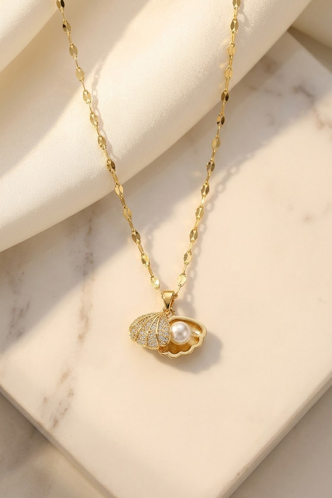 Lilyah Jewelry's 18k gold plated chain necklace with a shell-shaped pendant featuring a white pearl, displayed on a cream-colored marble surface with soft shadows.