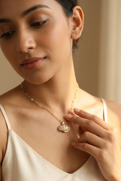 A woman wearing Lilyah Jewelry's delicate 18k gold plated chain necklace with a small shell pendant featuring a white pearl center, styled with a cream-colored satin top against a warm beige background.