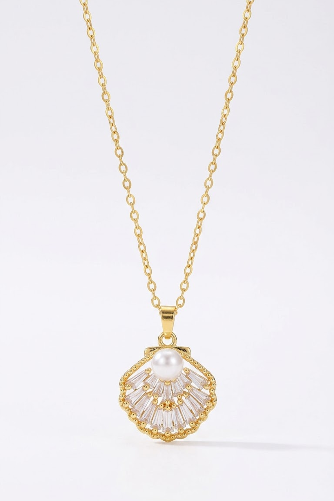 A gold chain necklace with a scallop-shaped pendant featuring a white pearl at the center and clear baguette-cut stones radiating from a gold setting, shown on a clean white background.