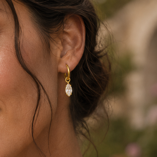 A close-up side profile of a woman wearing Lilyah Jewelry's delicate 18k gold plated hoop earring with a marquise-cut clear zircon dangle