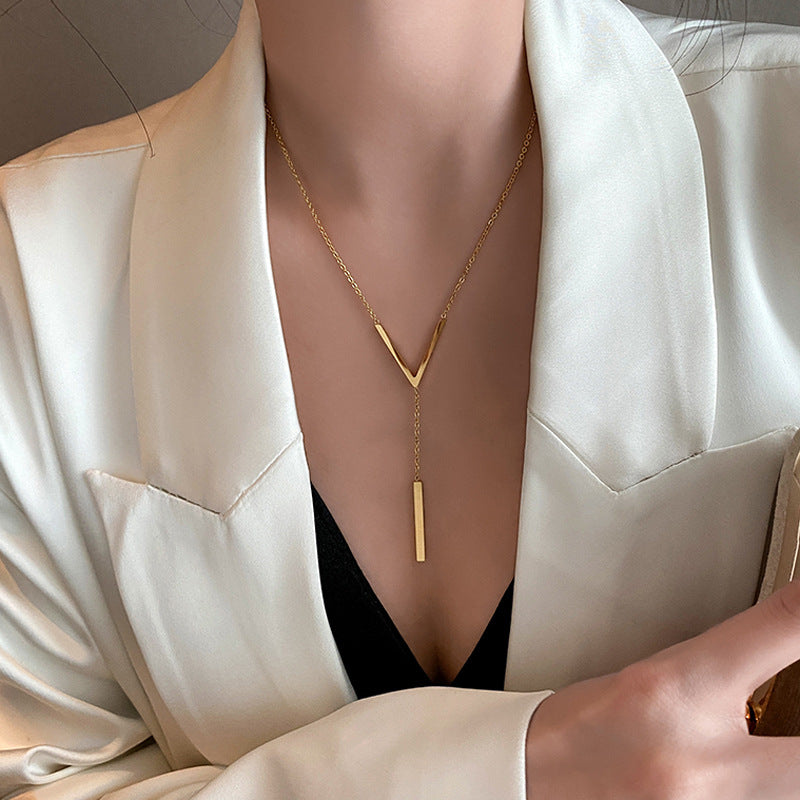 A person wearing a white blazer and a black top, showcasing a gold-plated minimalistic V-necklace. Lilyah Jewelry Gold Plated Necklace. Gift Ideas for her.