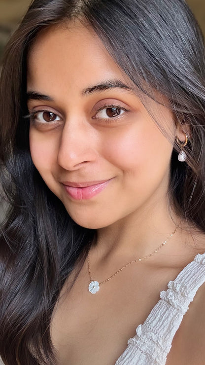 Woman with long dark hair wearing a white top and dainty gold necklace with a pretty white flower pendant that gives soft girl aesthetics. Pinteresty Picture.