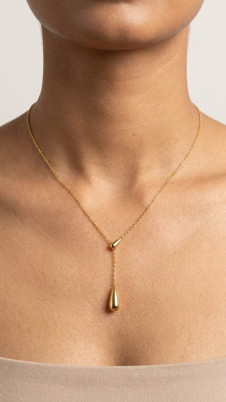 Lilyah Jewelry's Gold plated necklace with a golden drop pendant on a person wearing a beige top against a neutral background. the necklace is minimal and beautiful