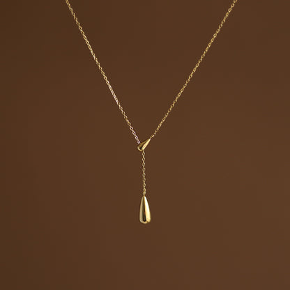 A gold-plated dainty golden water droplet necklace on a brown background. Lilyah Jewelry Gold Plated Necklace. Gift Ideas for her.